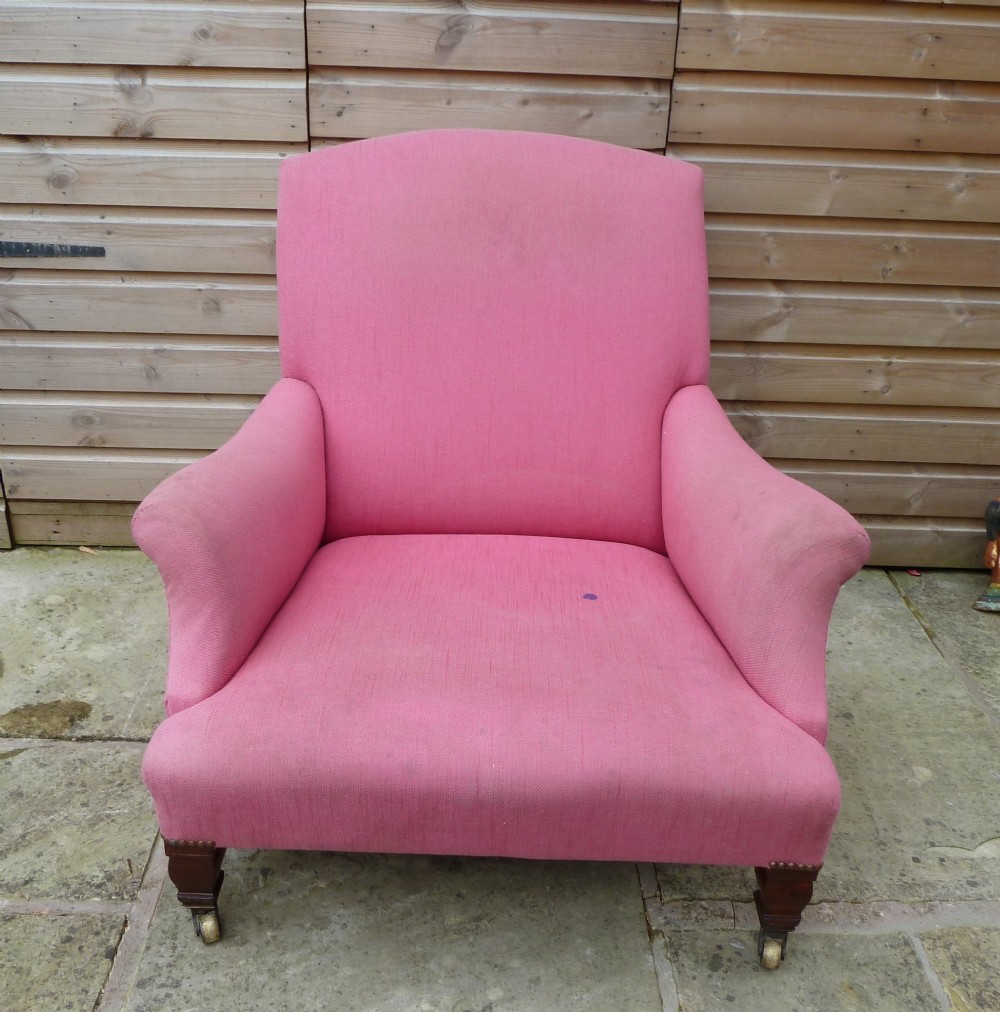 A deep-seated Howard style armchair upholstered in pink fabric, featuring low scrolled arms, turned mahogany front legs, and brass castors. View II