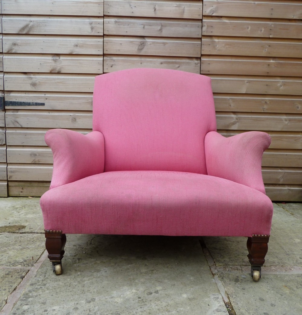 A deep-seated Howard style armchair upholstered in pink fabric, featuring low scrolled arms, turned mahogany front legs, and brass castors. View III