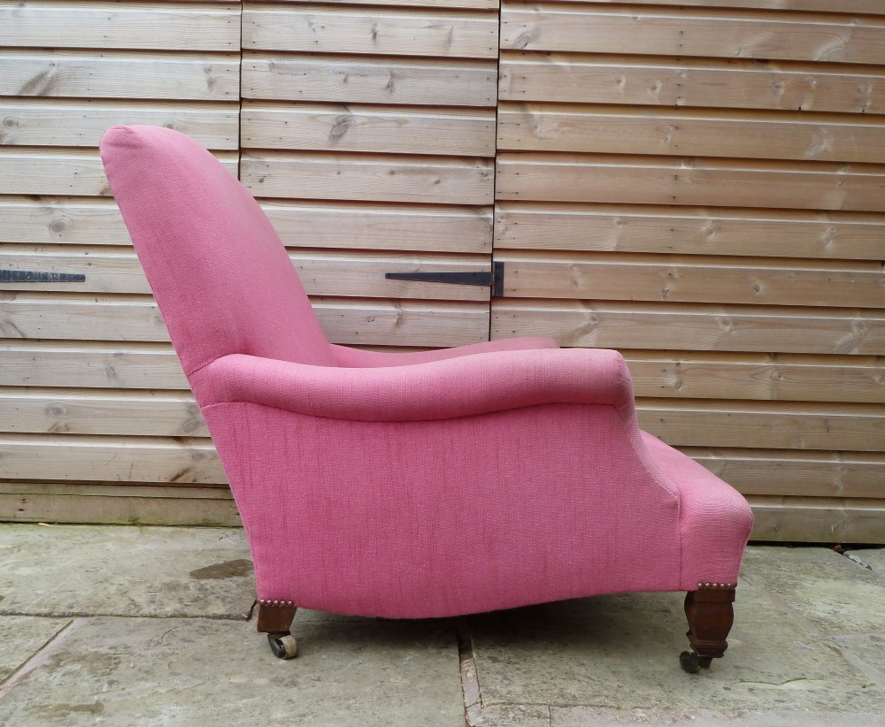 A deep-seated Howard style armchair upholstered in pink fabric, featuring low scrolled arms, turned mahogany front legs, and brass castors. View IV