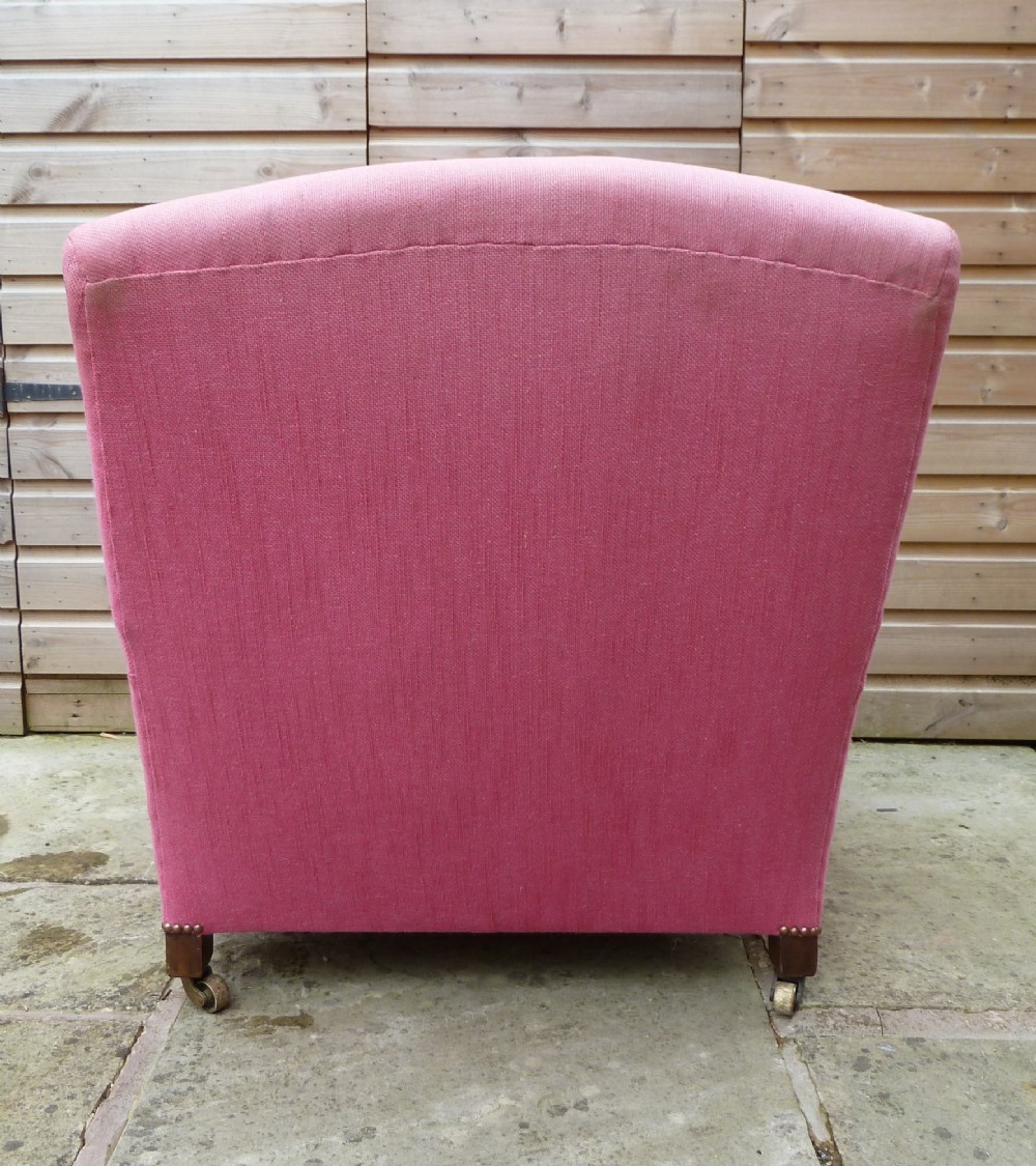 A deep-seated Howard style armchair upholstered in pink fabric, featuring low scrolled arms, turned mahogany front legs, and brass castors. View V