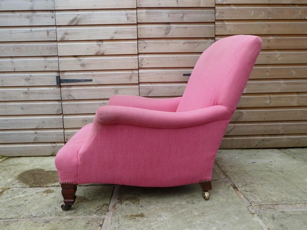 A deep-seated Howard style armchair upholstered in pink fabric, featuring low scrolled arms, turned mahogany front legs, and brass castors. View VI
