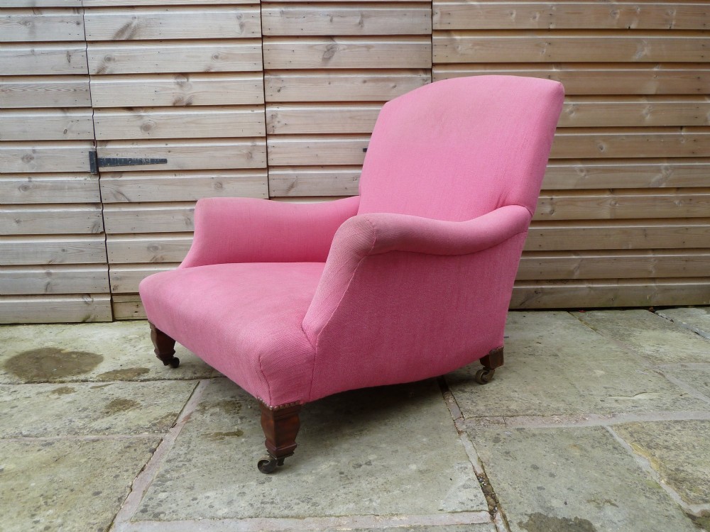 A deep-seated Howard style armchair upholstered in pink fabric, featuring low scrolled arms, turned mahogany front legs, and brass castors. View VII