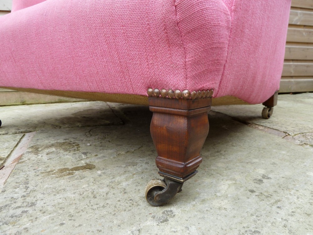 A deep-seated Howard style armchair upholstered in pink fabric, featuring low scrolled arms, turned mahogany front legs, and brass castors. View VIII