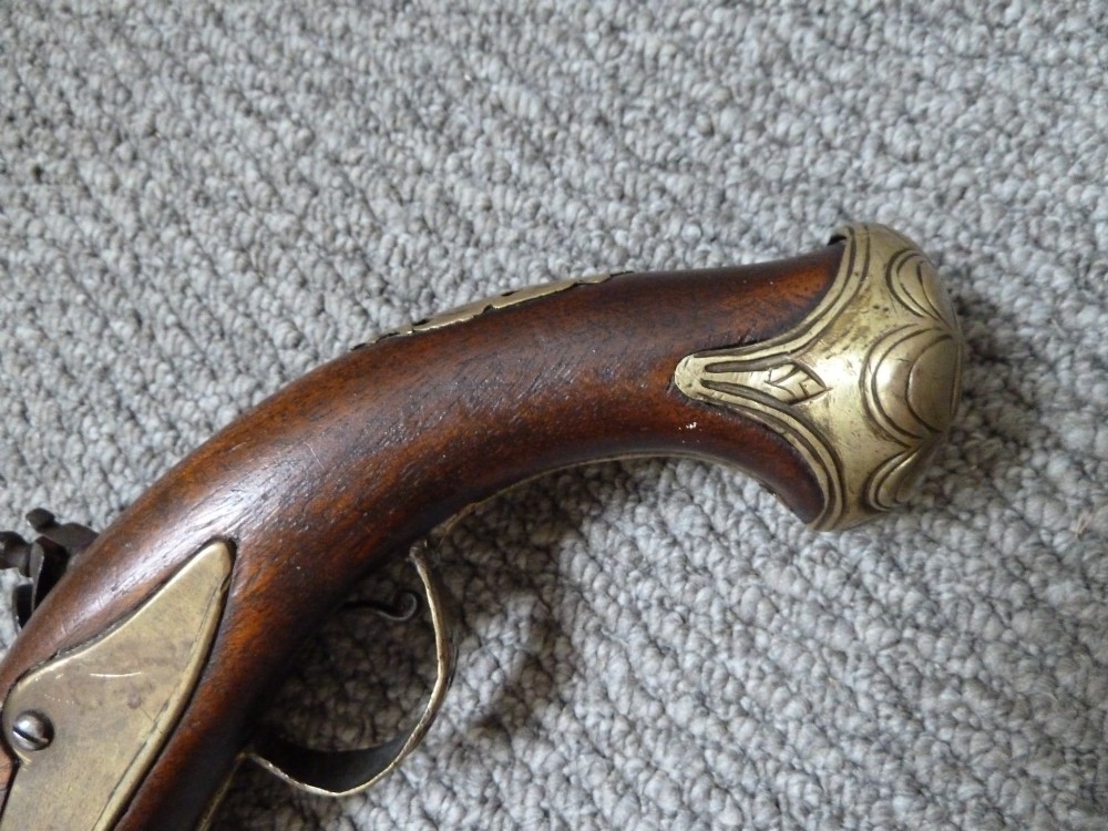 An 18th-century flintlock pistol featuring a carved dark walnut stock, engraved brass butt cap, brass ramrod pipes, and an iron lock mechanism. View III
