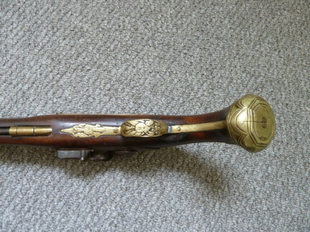 An 18th-century flintlock pistol featuring a carved dark walnut stock, engraved brass butt cap, brass ramrod pipes, and an iron lock mechanism. View IV