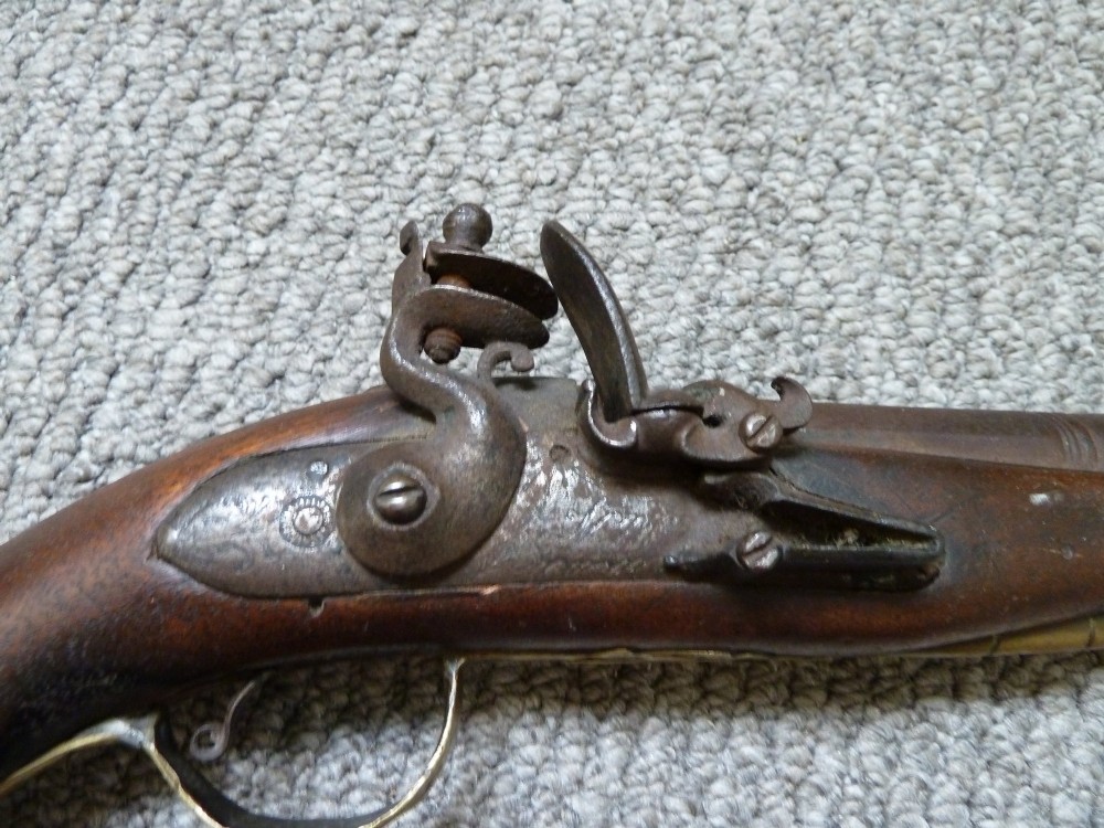 An 18th-century flintlock pistol featuring a carved dark walnut stock, engraved brass butt cap, brass ramrod pipes, and an iron lock mechanism. View V