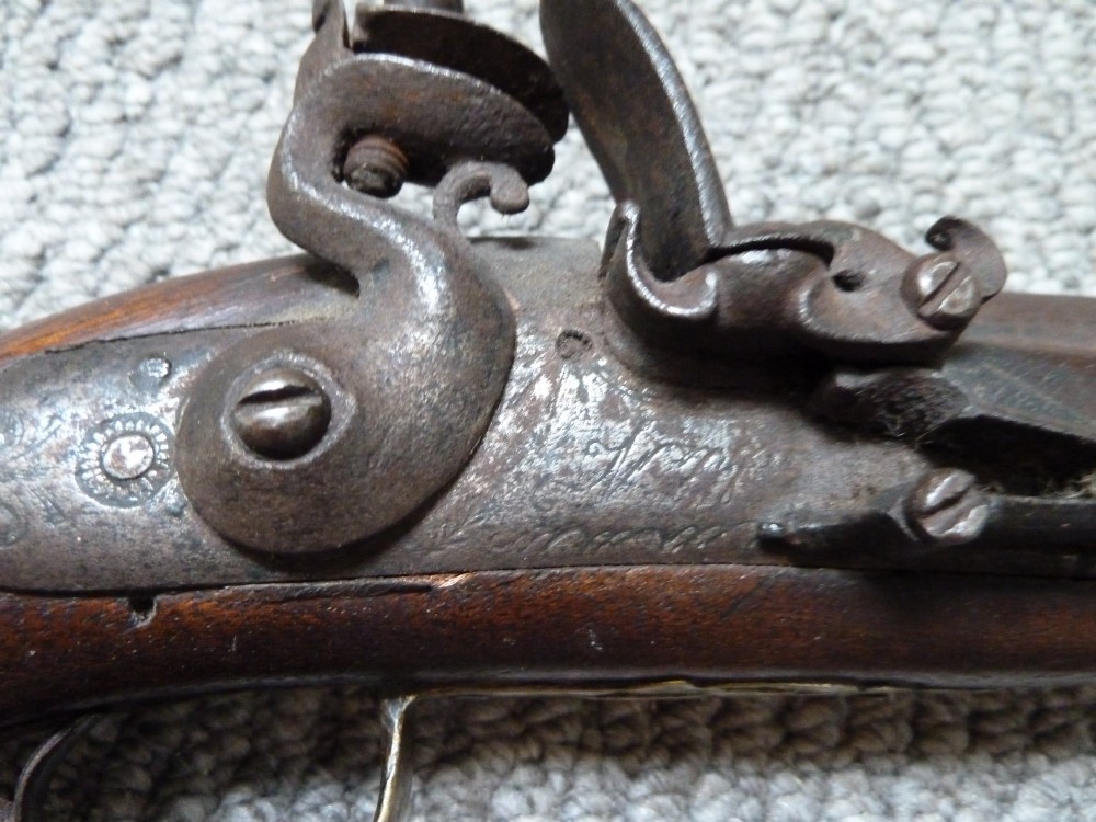 An 18th-century flintlock pistol featuring a carved dark walnut stock, engraved brass butt cap, brass ramrod pipes, and an iron lock mechanism. View VI