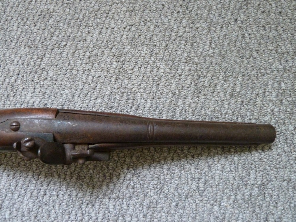 An 18th-century flintlock pistol featuring a carved dark walnut stock, engraved brass butt cap, brass ramrod pipes, and an iron lock mechanism. View VII