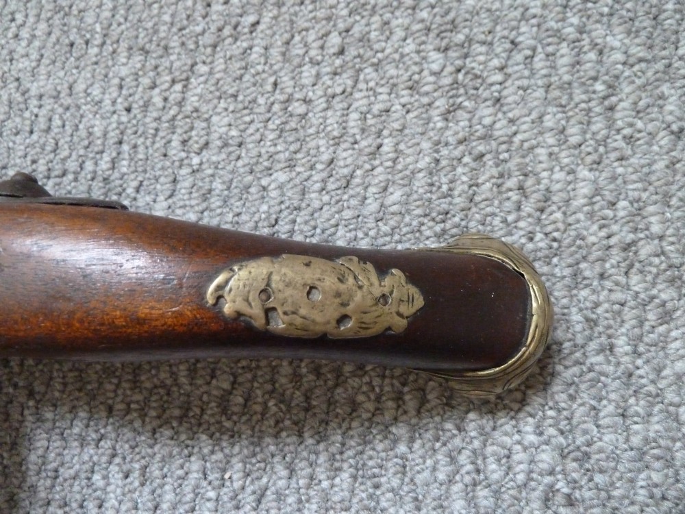 An 18th-century flintlock pistol featuring a carved dark walnut stock, engraved brass butt cap, brass ramrod pipes, and an iron lock mechanism. View VIII