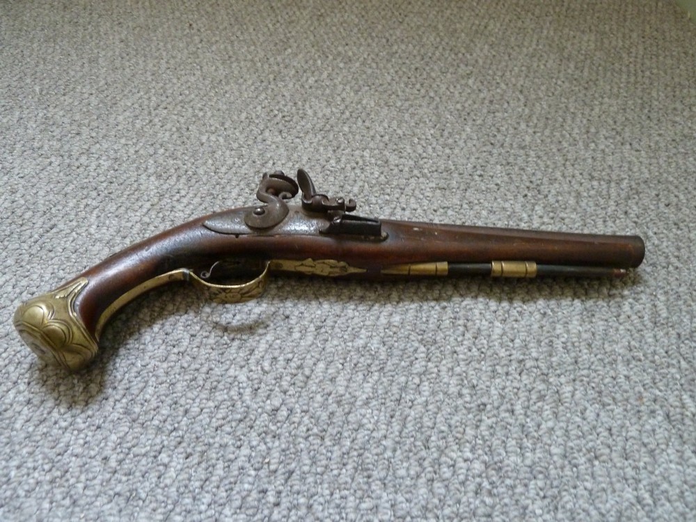 An 18th-century flintlock pistol featuring a carved dark walnut stock, engraved brass butt cap, brass ramrod pipes, and an iron lock mechanism. View XI