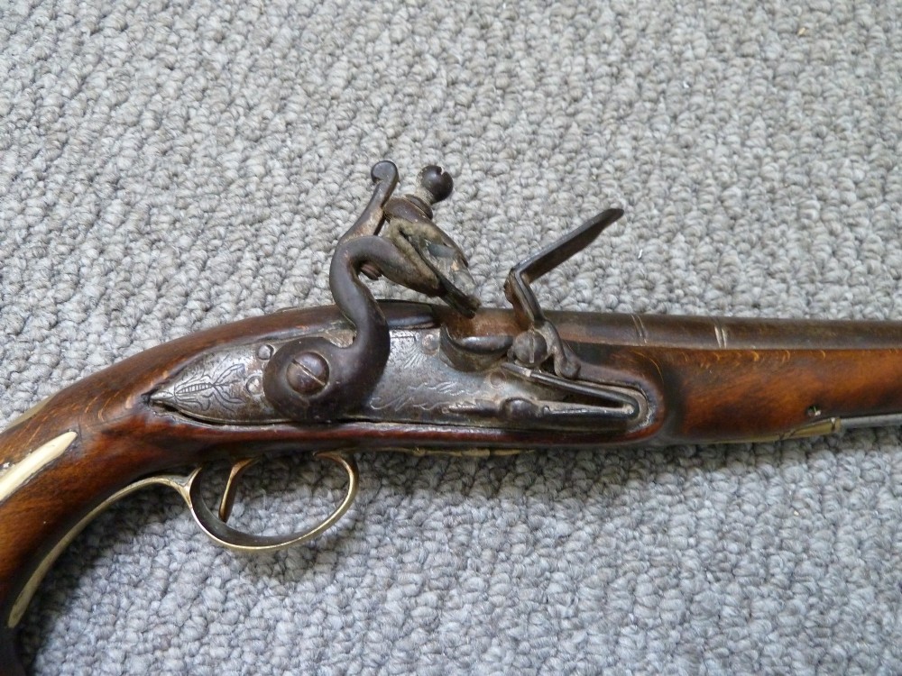 An 18th-century flintlock pistol featuring a dark walnut stock, engraved steel lock mechanism, and polished brass fittings. View III