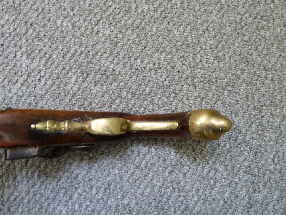 An 18th-century flintlock pistol featuring a dark walnut stock, engraved steel lock mechanism, and polished brass fittings. View IV