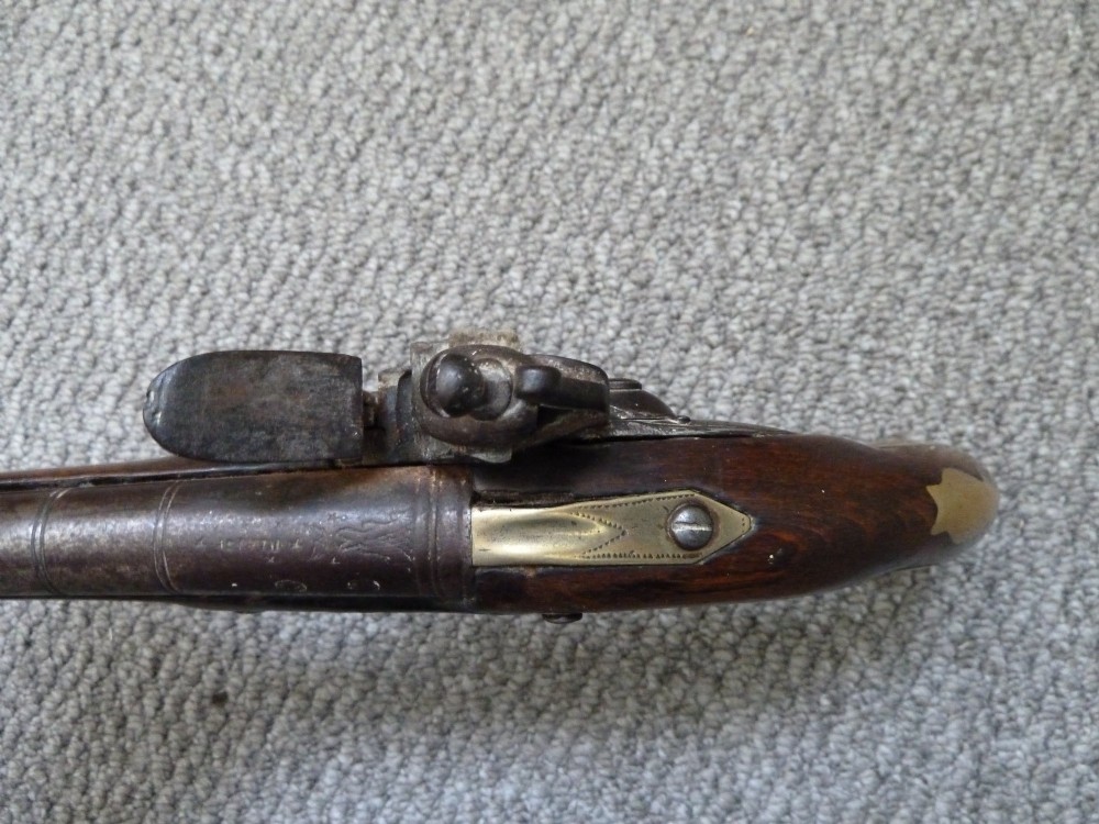 An 18th-century flintlock pistol featuring a dark walnut stock, engraved steel lock mechanism, and polished brass fittings. View V