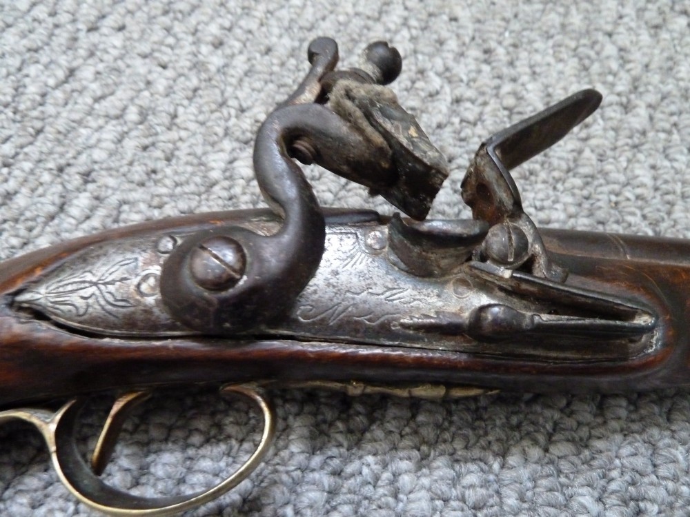 An 18th-century flintlock pistol featuring a dark walnut stock, engraved steel lock mechanism, and polished brass fittings. View VI