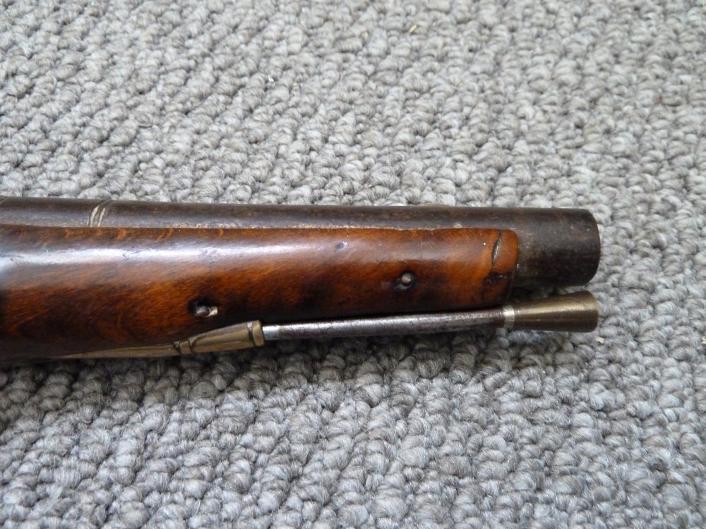 An 18th-century flintlock pistol featuring a dark walnut stock, engraved steel lock mechanism, and polished brass fittings. View VII