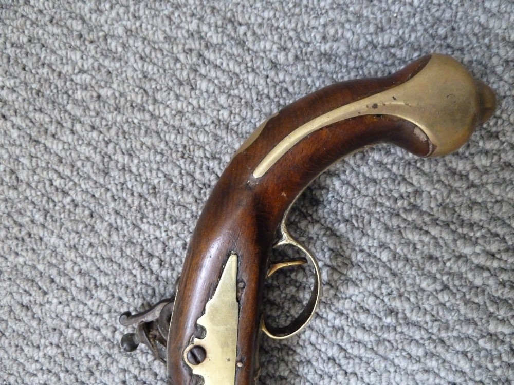 An 18th-century flintlock pistol featuring a dark walnut stock, engraved steel lock mechanism, and polished brass fittings. View IX
