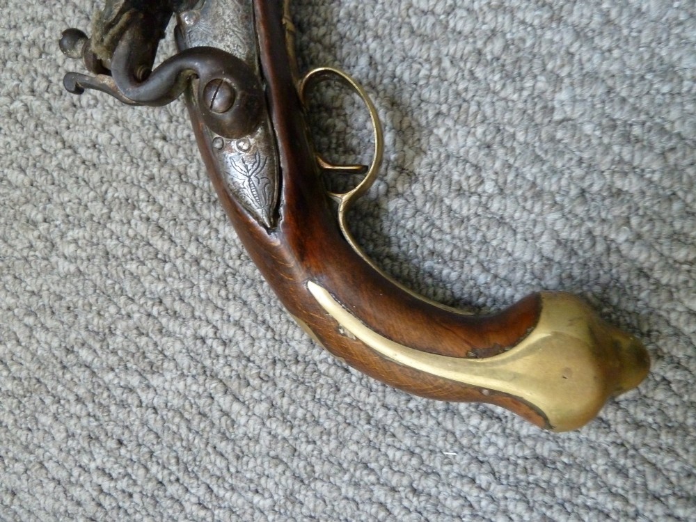 An 18th-century flintlock pistol featuring a dark walnut stock, engraved steel lock mechanism, and polished brass fittings. View X