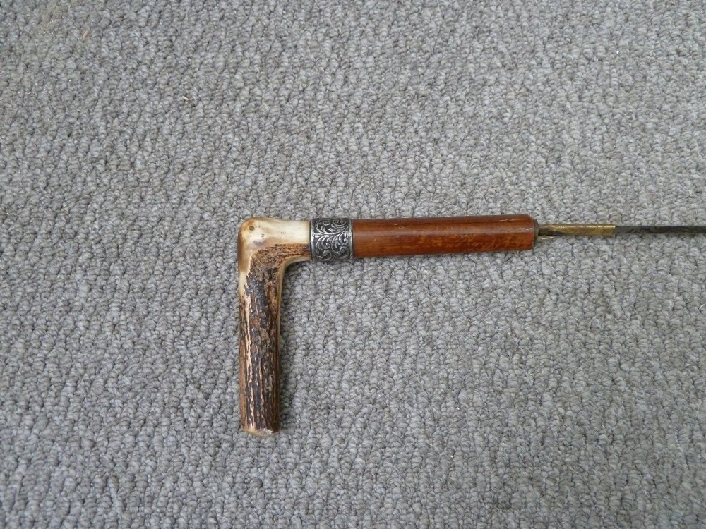 A Victorian sword stick displayed unsheathed in two parts, showcasing a stag horn handle, decorative metal ferrule, dark wooden scabbard, and a narrow steel blade. View II