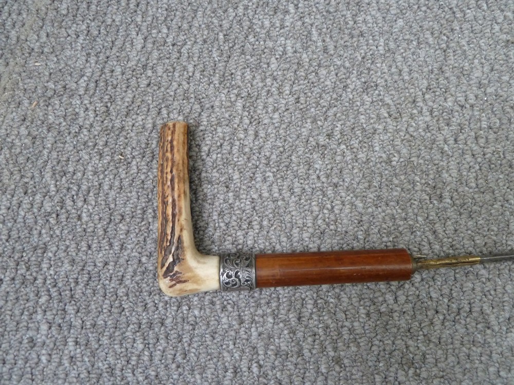 A Victorian sword stick displayed unsheathed in two parts, showcasing a stag horn handle, decorative metal ferrule, dark wooden scabbard, and a narrow steel blade. View III