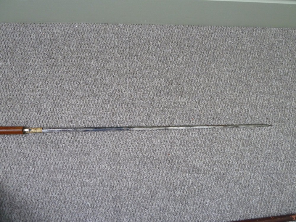A Victorian sword stick displayed unsheathed in two parts, showcasing a stag horn handle, decorative metal ferrule, dark wooden scabbard, and a narrow steel blade. View IV