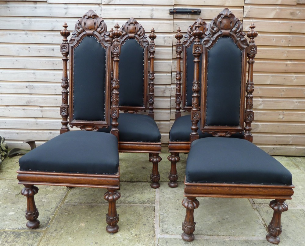 A set of four Victorian Gothic style carved oak high-back chairs featuring black upholstered seats and backrests with ornate cresting and turned legs. View II