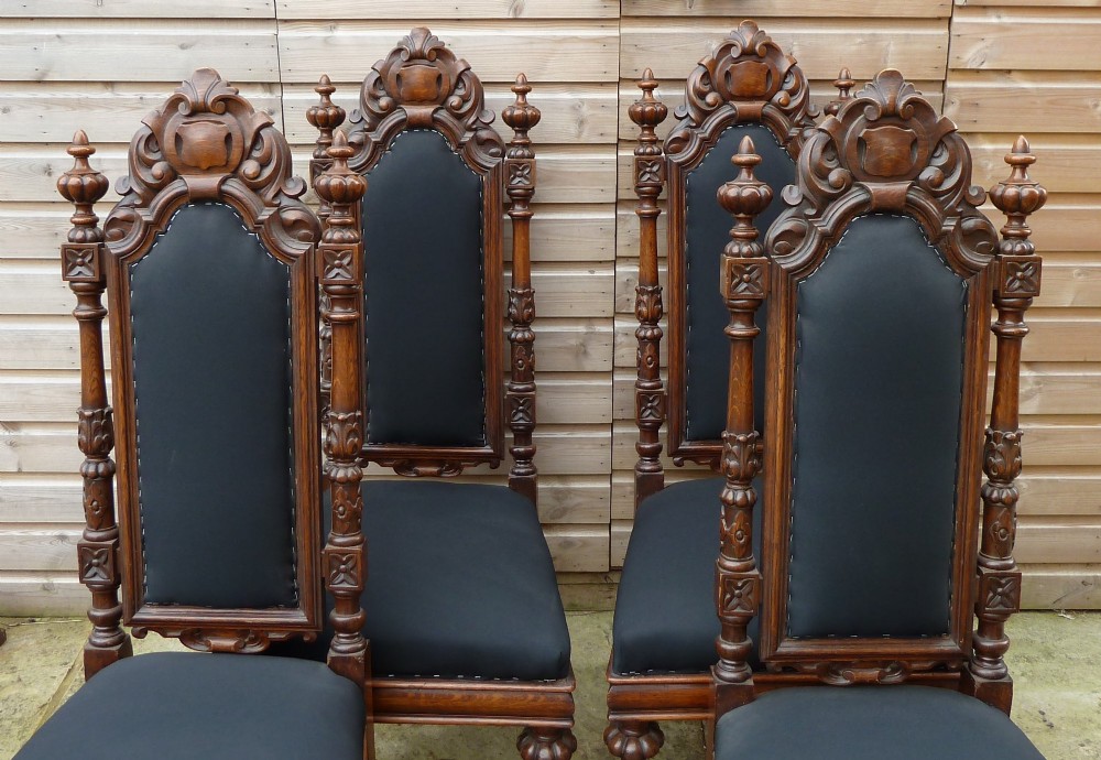 A set of four Victorian Gothic style carved oak high-back chairs featuring black upholstered seats and backrests with ornate cresting and turned legs. View III