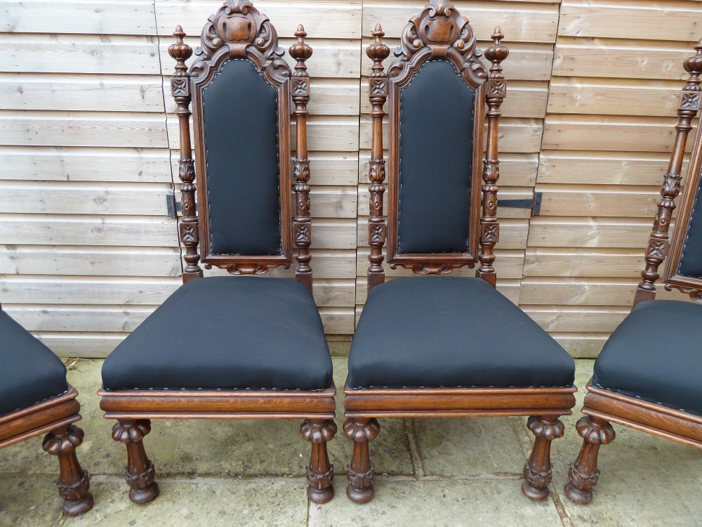 A set of four Victorian Gothic style carved oak high-back chairs featuring black upholstered seats and backrests with ornate cresting and turned legs. View IV
