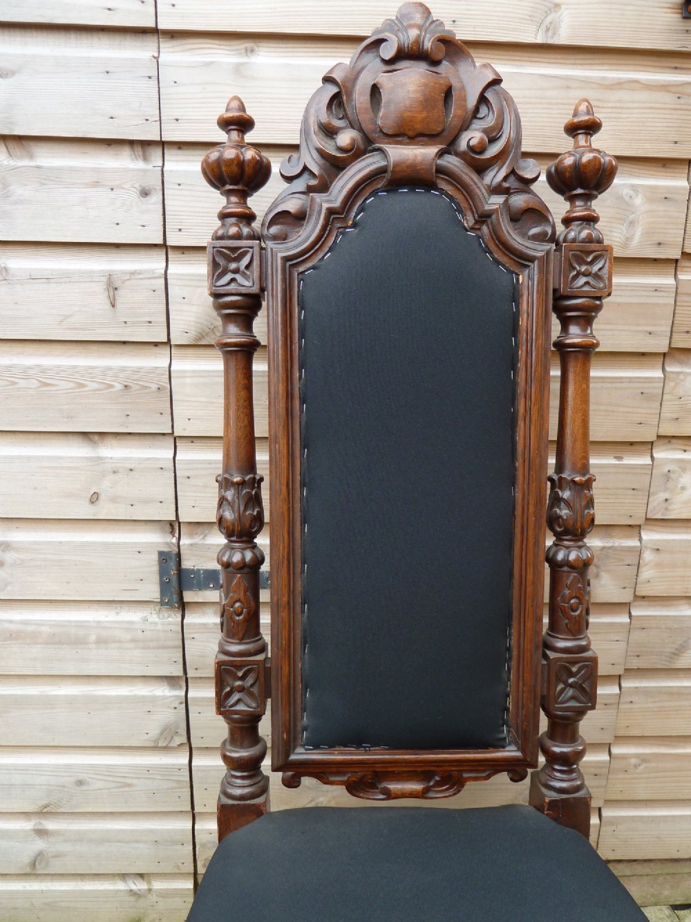 A set of four Victorian Gothic style carved oak high-back chairs featuring black upholstered seats and backrests with ornate cresting and turned legs. View VI