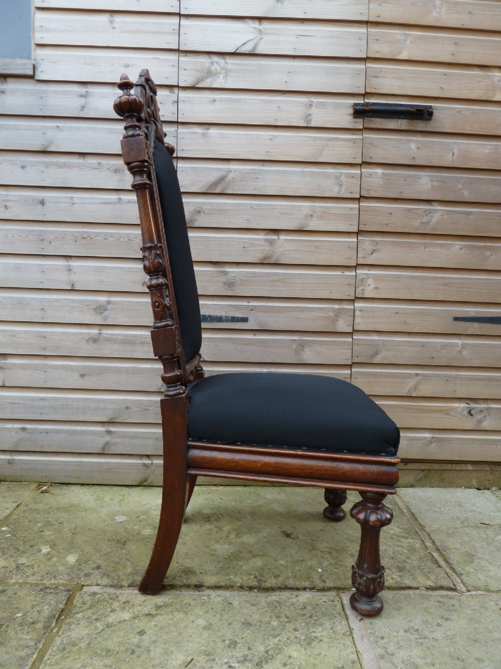 A set of four Victorian Gothic style carved oak high-back chairs featuring black upholstered seats and backrests with ornate cresting and turned legs. View VII