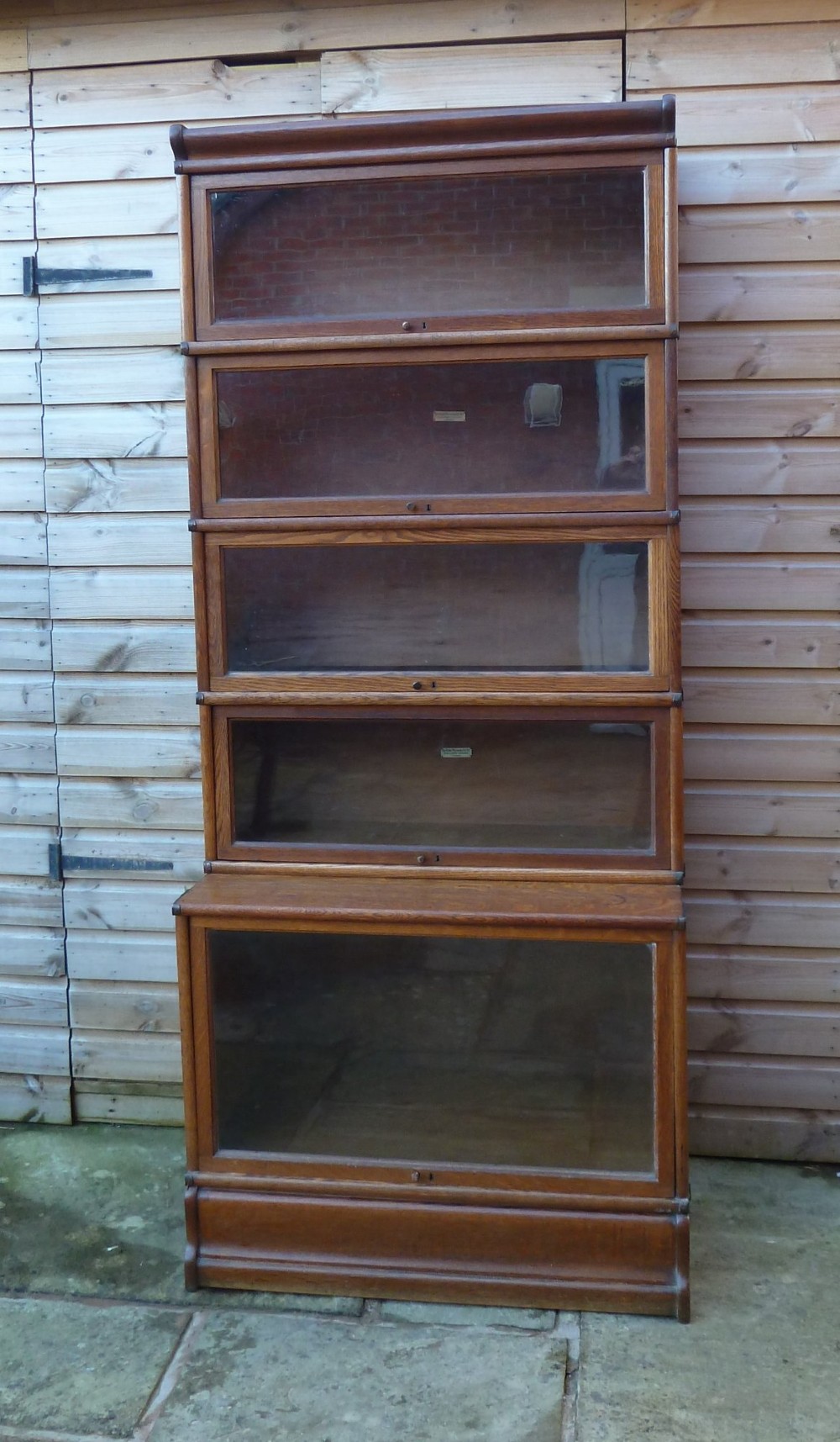 A tall five-tier golden oak Globe Wernicke sectional bookcase featuring glass lift-up doors and a deeper base unit. View II
