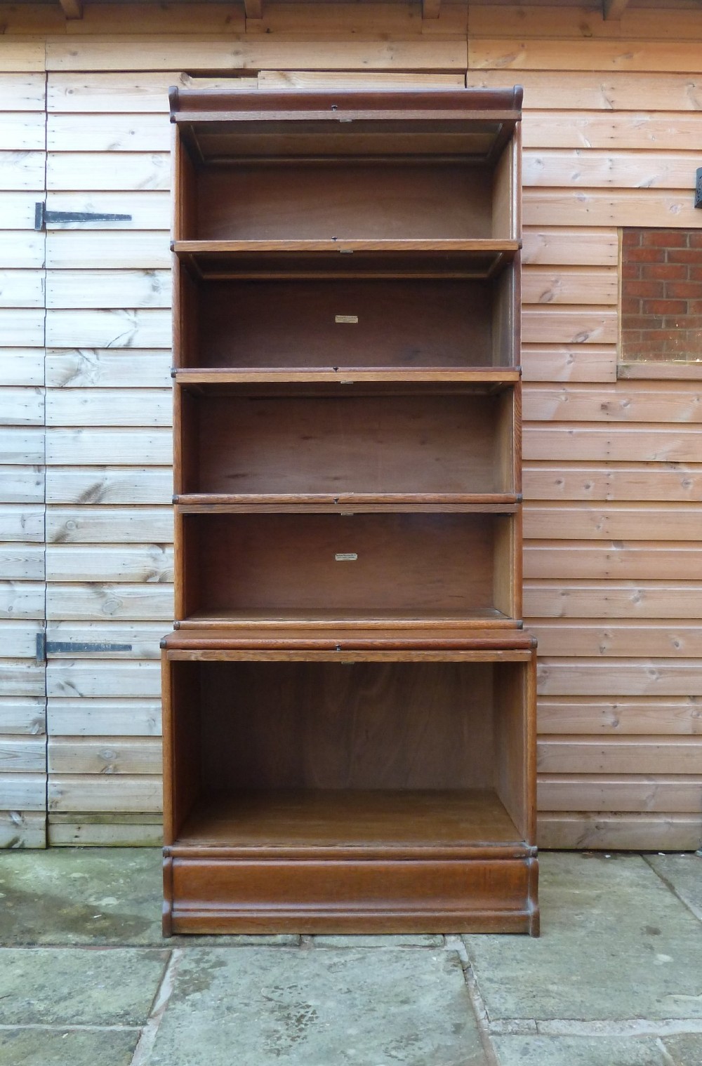 A tall five-tier golden oak Globe Wernicke sectional bookcase featuring glass lift-up doors and a deeper base unit. View X