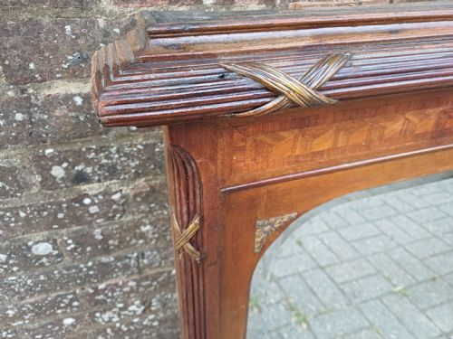 fig 4. A large Edwardian wooden overmantel mirror featuring marquetry inlay, a reeded frame with gilded cross-ribbon details, and an arched upper glass line.
