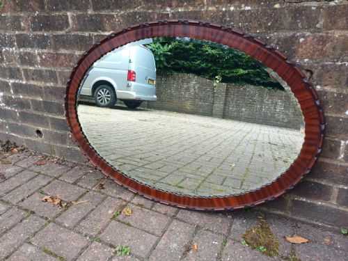 fig 1. A large horizontal oval wall mirror featuring a carved mahogany wooden frame and a bevelled glass edge.