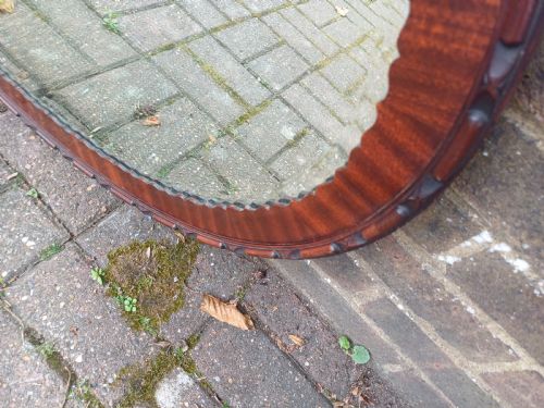 fig 5. A large horizontal oval wall mirror featuring a carved mahogany wooden frame and a bevelled glass edge.