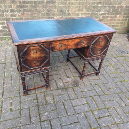 fig 1. A vintage dark oak writing desk with five drawers, geometric bead moulding, turned legs, brass handles, and a black leather inset top.