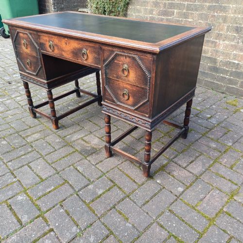 fig 5. A vintage dark oak writing desk with five drawers, geometric bead moulding, turned legs, brass handles, and a black leather inset top.