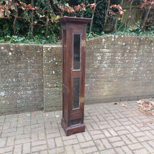 fig 1. A tall, narrow Victorian dark oak gun cupboard featuring two glass panels set into a single front door with decorative brass hinges.