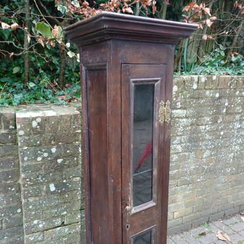 fig 2. A tall, narrow Victorian dark oak gun cupboard featuring two glass panels set into a single front door with decorative brass hinges.
