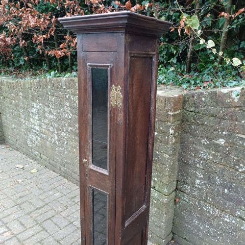 fig 4. A tall, narrow Victorian dark oak gun cupboard featuring two glass panels set into a single front door with decorative brass hinges.