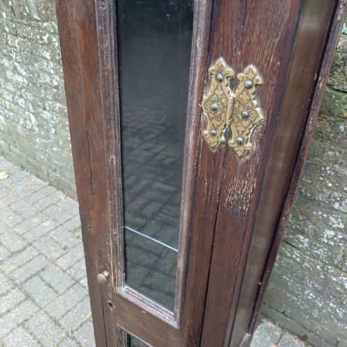 fig 6. A tall, narrow Victorian dark oak gun cupboard featuring two glass panels set into a single front door with decorative brass hinges.