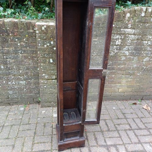 fig 7. A tall, narrow Victorian dark oak gun cupboard featuring two glass panels set into a single front door with decorative brass hinges.
