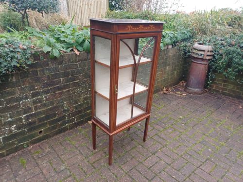 fig 2. An Edwardian mahogany display cabinet featuring a glazed single door with curved glazing bars, satinwood marquetry inlay, fabric-lined shelves, and tapered square legs.