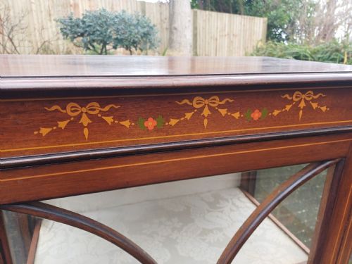 fig 4. An Edwardian mahogany display cabinet featuring a glazed single door with curved glazing bars, satinwood marquetry inlay, fabric-lined shelves, and tapered square legs.