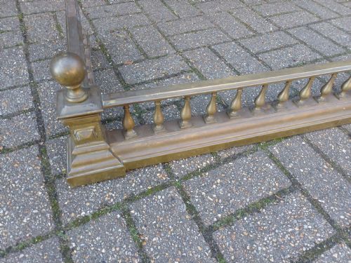 fig 3. An antique brass fireplace fender featuring a turned spindle balustrade, spherical corner finials, and a stepped plinth base.