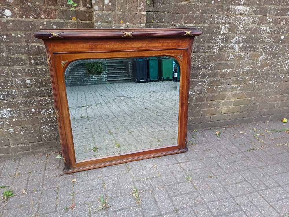 A large Edwardian wooden overmantel mirror featuring marquetry inlay, a reeded frame with gilded cross-ribbon details, and an arched upper glass line.