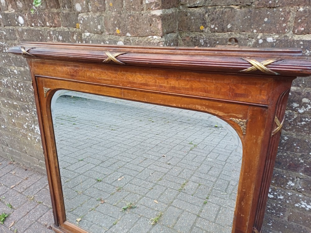 A large Edwardian wooden overmantel mirror featuring marquetry inlay, a reeded frame with gilded cross-ribbon details, and an arched upper glass line. View IV