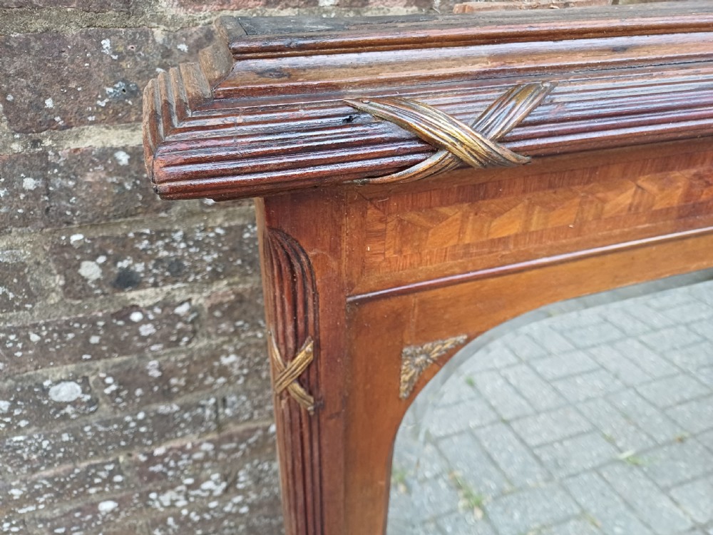 A large Edwardian wooden overmantel mirror featuring marquetry inlay, a reeded frame with gilded cross-ribbon details, and an arched upper glass line. View V