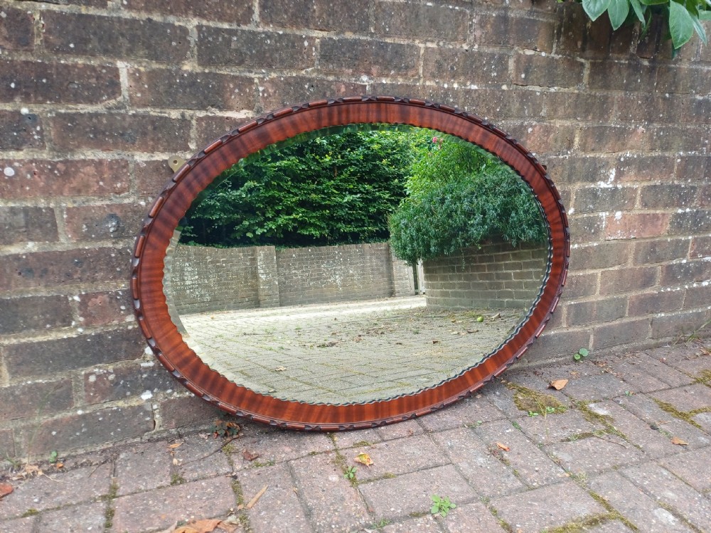 A large horizontal oval wall mirror featuring a carved mahogany wooden frame and a bevelled glass edge.