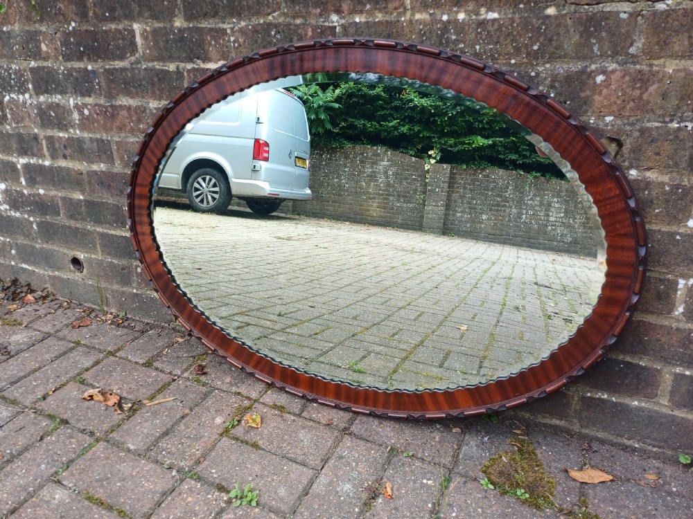 A large horizontal oval wall mirror featuring a carved mahogany wooden frame and a bevelled glass edge. View II