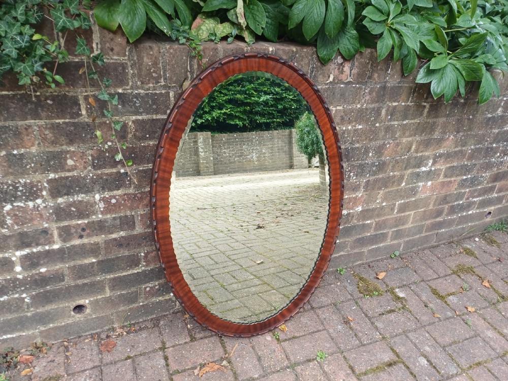 A large horizontal oval wall mirror featuring a carved mahogany wooden frame and a bevelled glass edge. View X